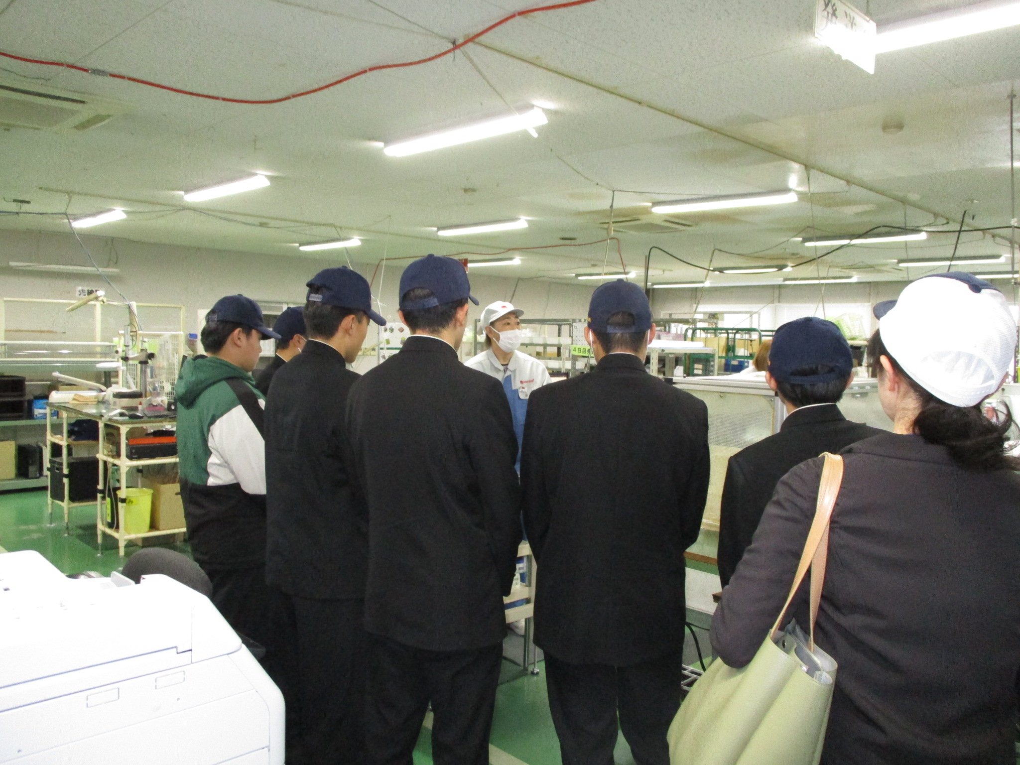 工場の製品発送工程を見学する高校生の後ろ姿